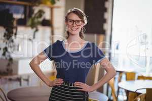Portrait of confident young waitress standing with hands on hip
