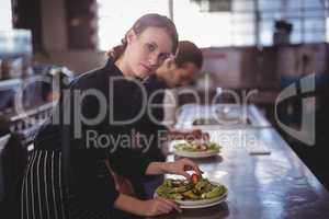 Portrait of confident waitress preparing salad at counter with waiter