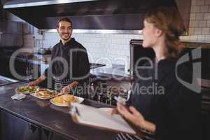 Young waiter preparing food while looking at waitress