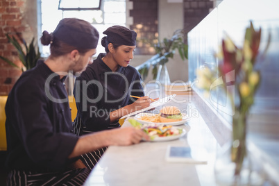 Young wait staff sitting with clipboard and food at counter