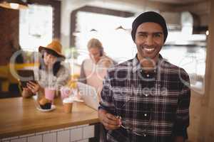 Portrait of smiling young man holding eyeglasses standing against female friends at coffee shop