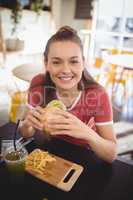 Portrait of smiling young gorgeous woman eating burger at coffee shop