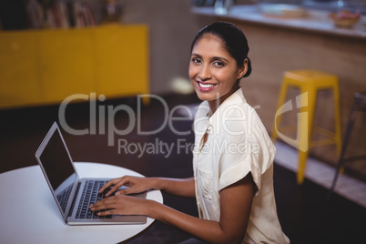 Side view portrait of smiling young woman using laptop at coffee shop
