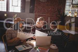 Young creative team discussing over papers while sitting at table