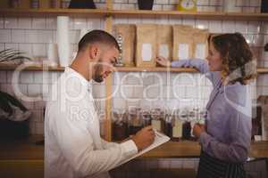 Male owner writing on clipboard while waitress arranging products