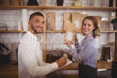 Portrait of smiling male owner and waitress arranging packages on shelf