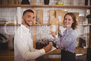 Portrait of smiling male owner and waitress arranging packages on shelf