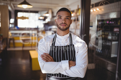 Portrait of young handsome waiter standing with arms crossed