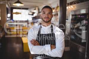 Portrait of young handsome waiter standing with arms crossed