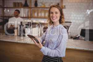 Smiling young waitress using digital tablet while standing by counter