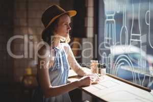 Thoughtful young woman wearing hat looking through window