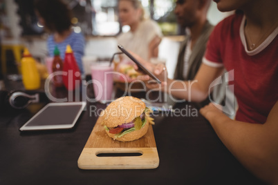 Midsection of young woman using smartphone while sitting with burger