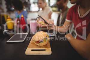 Midsection of young woman using smartphone while sitting with burger