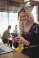 Smiling young woman texting through mobile phone at coffee shop