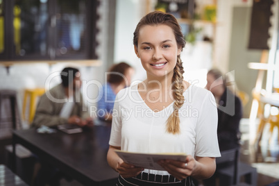 Smiling young waitress with menu at cafe