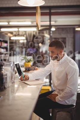 Side view of young male owner writing on notepad at counter