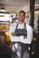 Portrait of smiling handsome young waiter standing with arms crossed