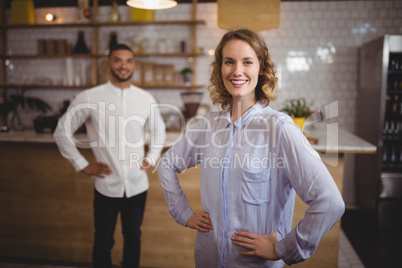 Smiling young woman with hand on hip against friend at coffee shop