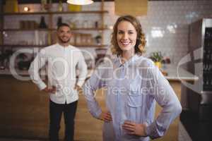 Smiling young woman with hand on hip against friend at coffee shop