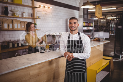 Portrait of waiter standing by counter at coffee shop