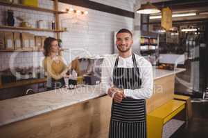 Portrait of waiter standing by counter at coffee shop
