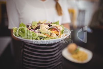 Midsection of waitress holding fresh Greek salad in plate