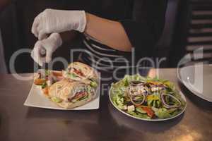 Midsection of female chef with fresh burgers and salad in plate on counter