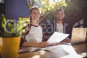 Portrait of smiling young creative professionals sitting with laptop at coffee shop