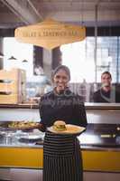 Portrait of smiling young waitress serving food while standing against waiter