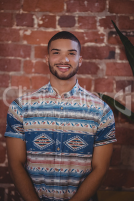 Portrait of smiling young male customer standing against brick wall