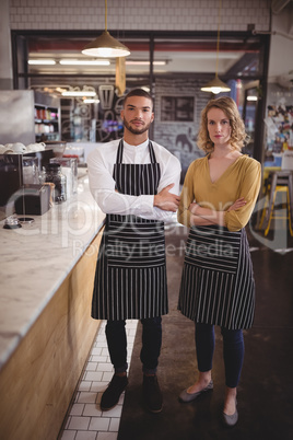 Portrait of confident young wait staff standing with arms crossed by counter