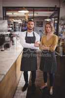 Portrait of confident young wait staff standing with arms crossed by counter