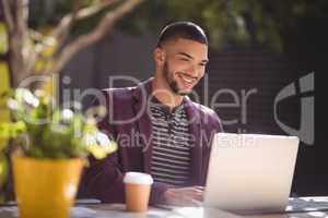 Smiling young man using laptop while sitting at coffee shop