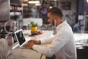 Side view of young male owner using laptop at counter
