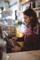Side view of young waiter with long hair using cash register at counter