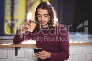 Young handsome man drinking coffee while using smartphone