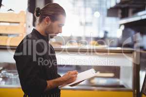 Side view of young waiter writing on clipboard