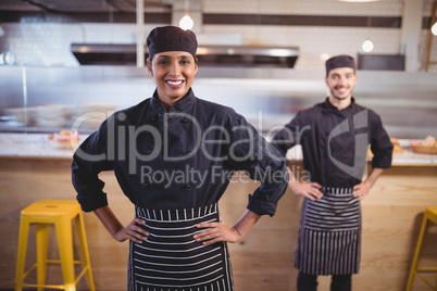 Portrait of smiling young wait staff standing with hands on hip against counter