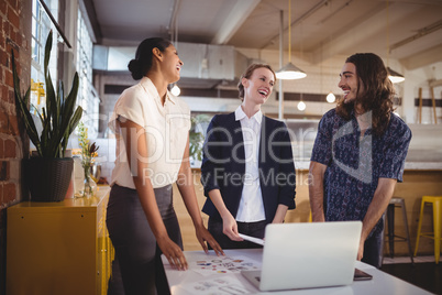 Cheerful young creative team standing by laptop on table