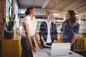 Cheerful young creative team standing by laptop on table