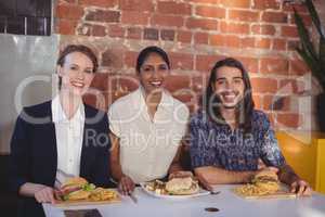 Portrait of smiling young friends sitting with food against brick wall