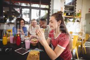 Beautiful young woman eating burger while sitting at coffee shop