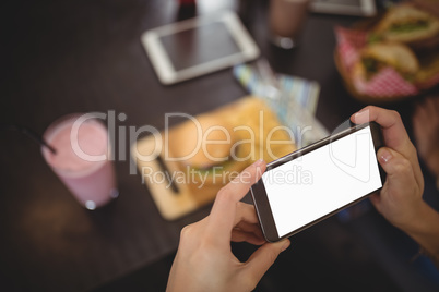 Cropped hands of woman photographing burger and milkshake at cafe