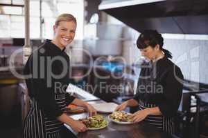 Portrait of smiling female chefs preparing fresh Greek salad at kitchen counter