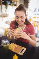 Smiling young gorgeous woman eating burger at coffee shop