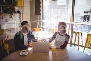 Smiling young friends talking while sitting with laptop at coffee shop