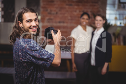 Smiling young photographer photographing female colleagues