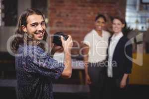 Smiling young photographer photographing female colleagues