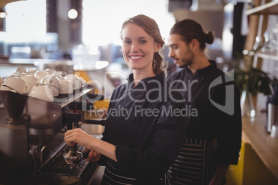 Portrait of smiling female barista using espresso maker against waiter