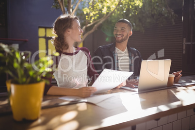 Smiling young creative professionals talking while sitting with laptop at coffee shop